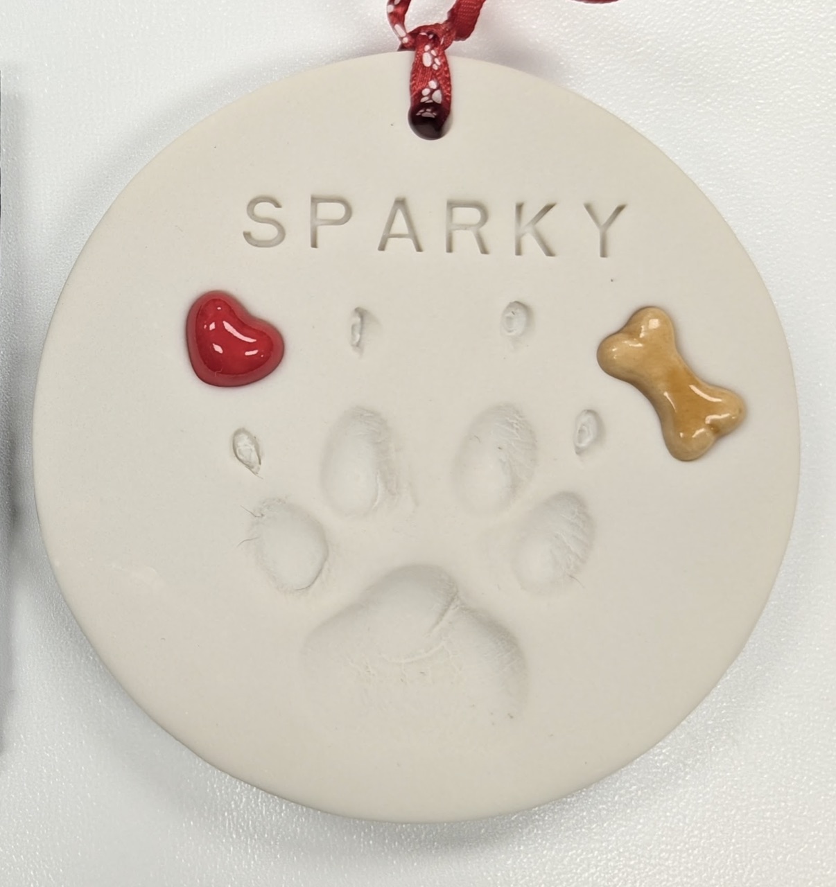 A generic mass-produced clay disc keepsake stamped with a pet's name and paw print